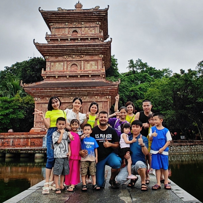 Travel group with local families posing in front of a traditional brick pagoda in Vietnam