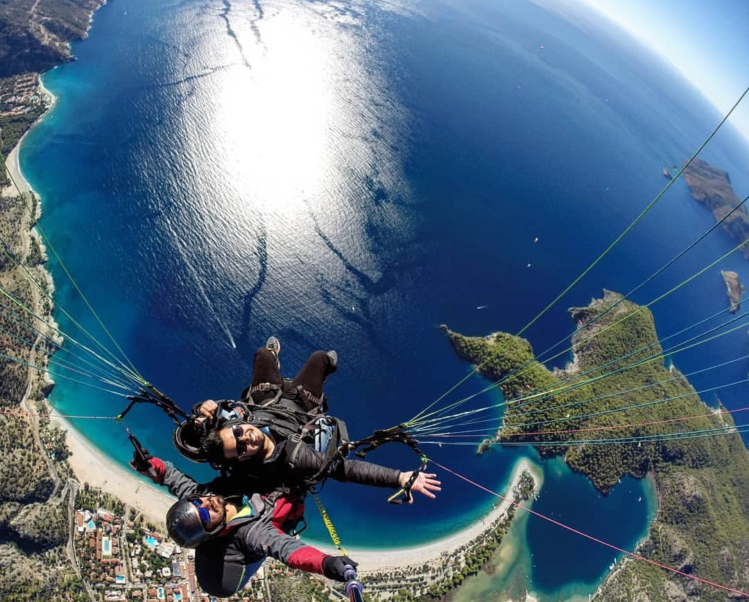 Tandem paragliding above a blue sea and curved coastline